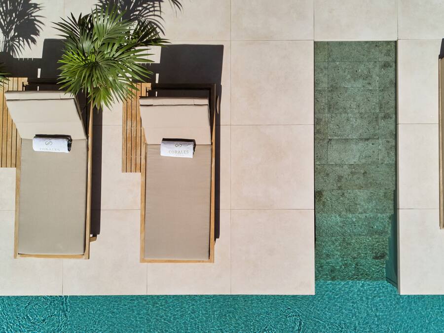 A poolside area with two sun loungers labeled "COWAYS" and "CORALES," a wooden signboard, and a green door.