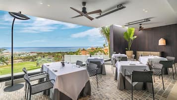 Un restaurante con terraza al aire libre que ofrece vistas panorámicas del océano y un campo de golf.