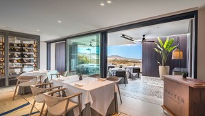 A modern dining area with tables and chairs, a reception desk, and a large window offering a view of the landscape.