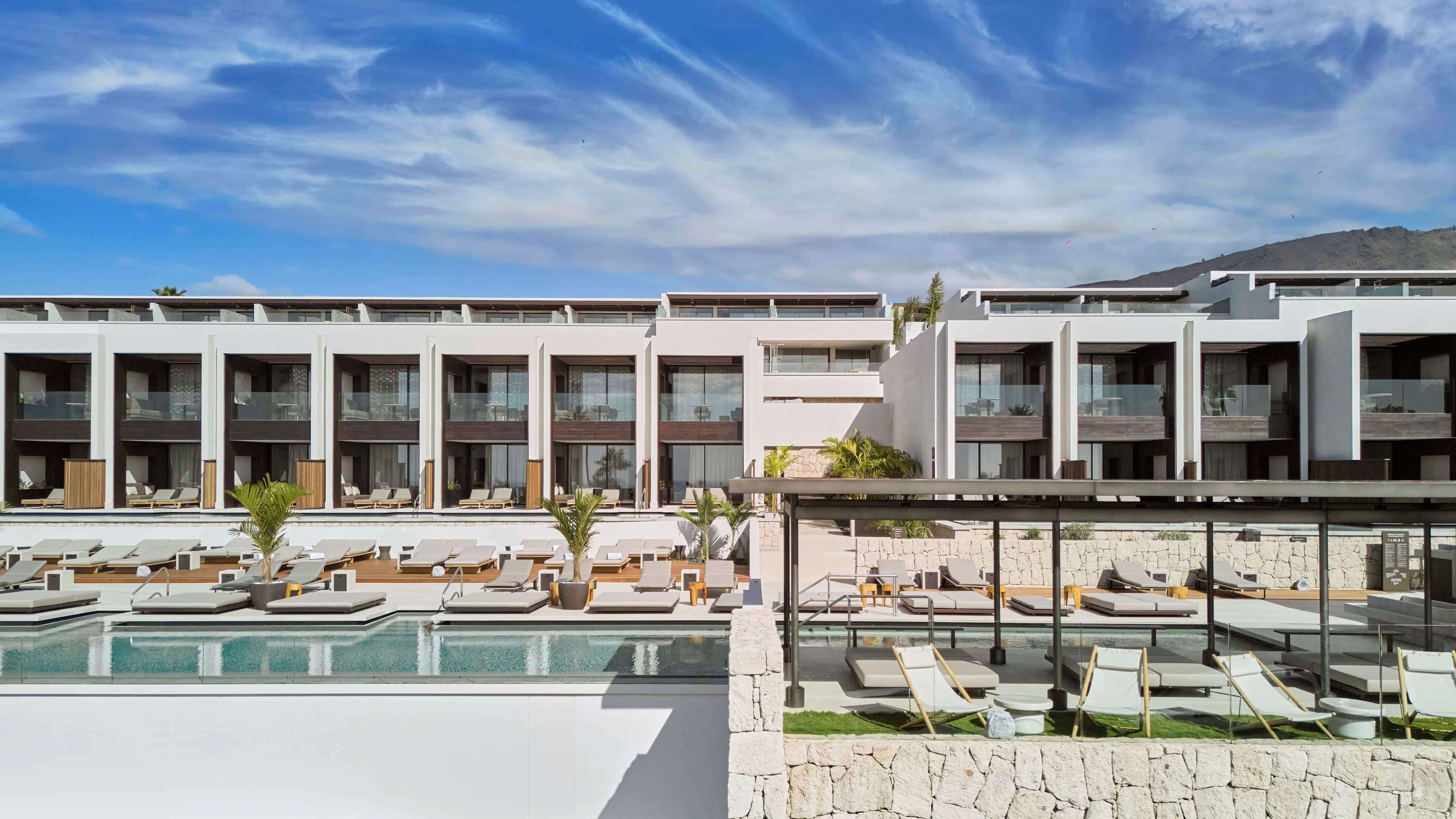 A modern hotel with multiple balconies, a swimming pool, and lounge areas.