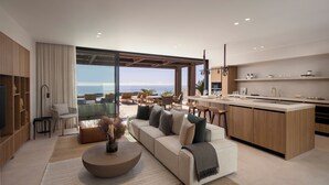 A modern living room with a large sofa, a coffee table, and a view of the ocean.