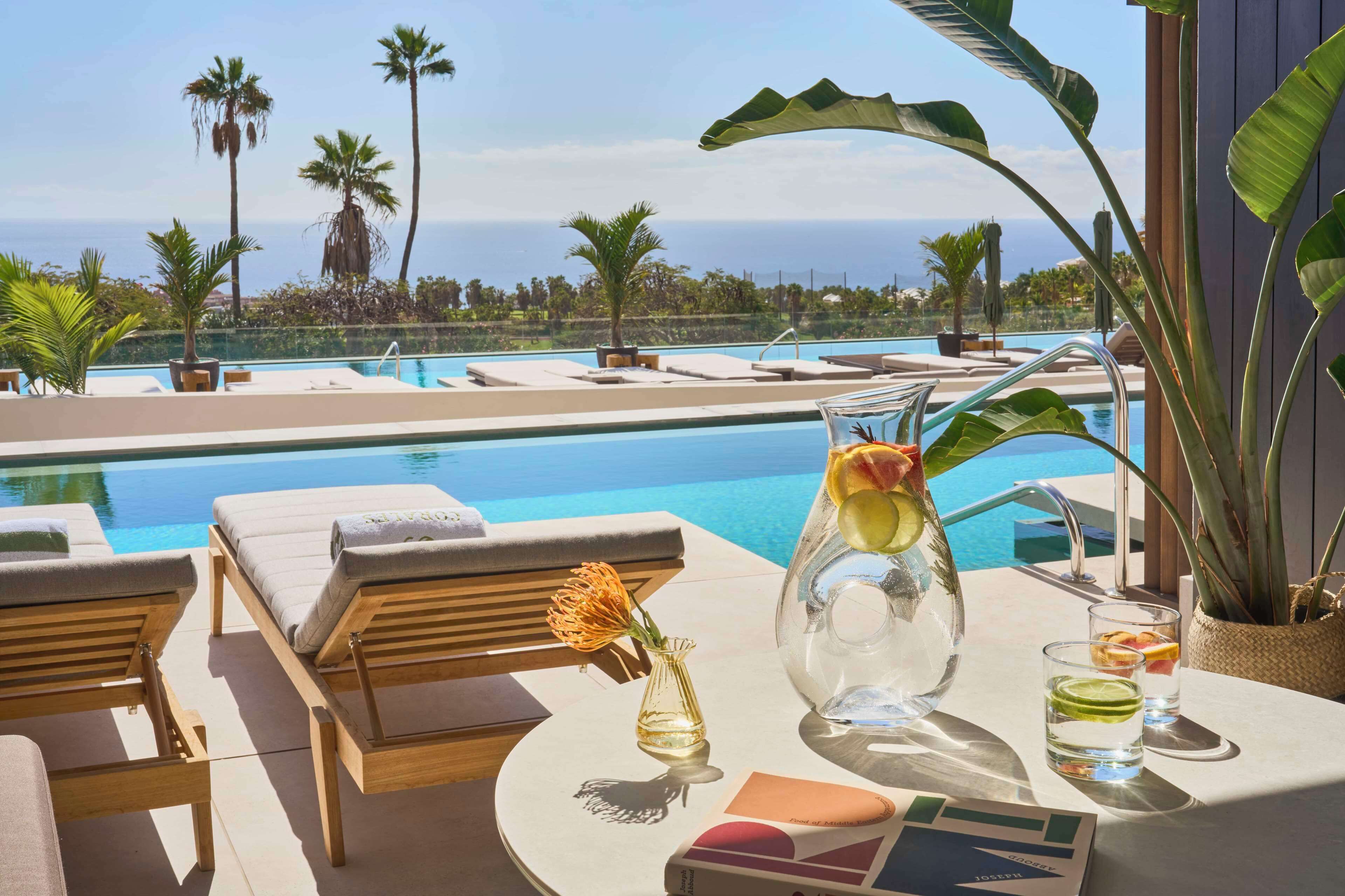 A poolside area with lounge chairs, a table with a pitcher of iced tea, and a view of the ocean.