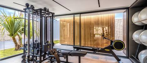 A modern gym with exercise equipment, a bench, and a view of a wooden wall and outdoor area.
