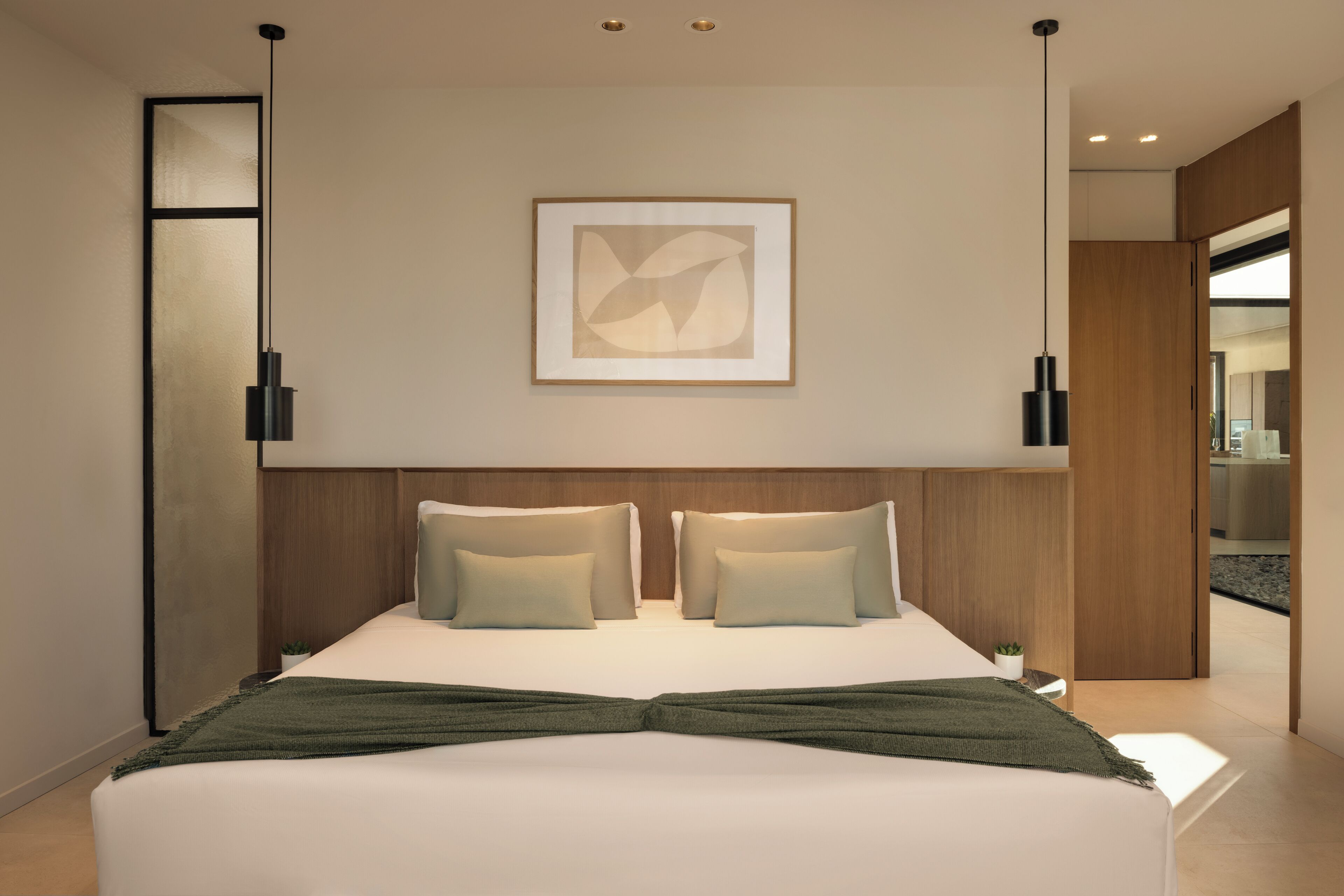 Une chambre d’hôtel moderne avec un grand lit, deux tables de chevet, une œuvre d’art abstraite encadrée au mur et une tête de lit en bois.