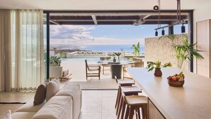 A modern living room with a sofa, dining area, and a view of the sea.