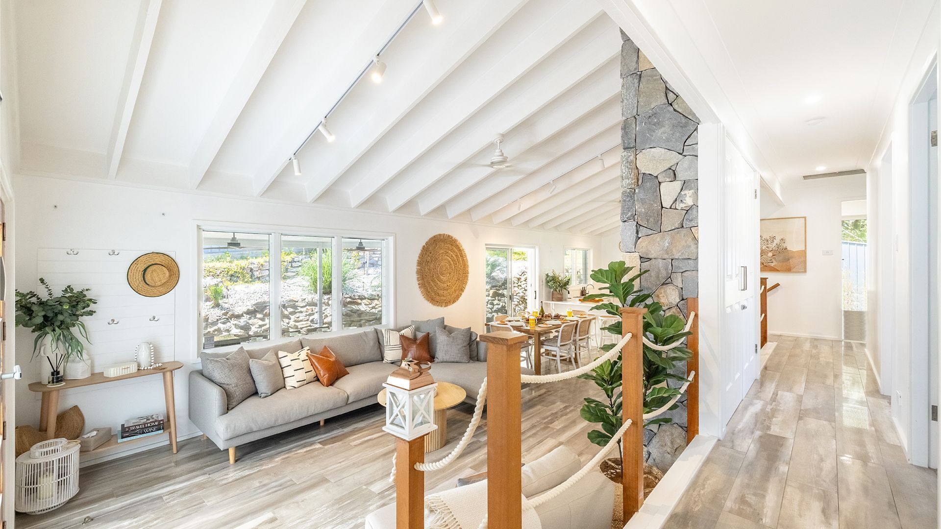 A spacious living area with a high ceiling, a stone accent wall, and a view of a garden through large windows.