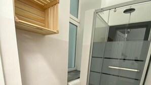 Un pasillo estrecho con un estante de madera, mampara de ducha de vidrio y un radiador.