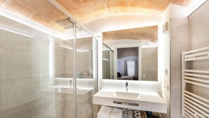 Un baño moderno con cabina de ducha de vidrio, un espejo grande y un tocador blanco con perchero.