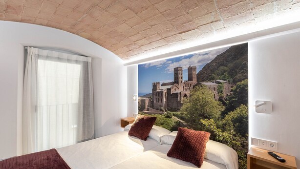 Habitación de hotel con una cama grande, dos almohadas, una mesita de noche y un televisor montado en la pared.