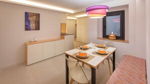 Un comedor moderno con una mesa de madera preparada para cuatro personas, una lámpara colgante colorida y una ventana con vistas.