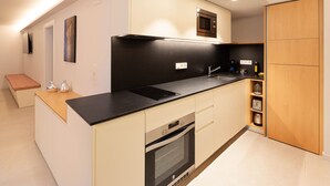 Cocina compacta con encimera negra, horno integrado y microondas. Cuenta con un mueble de madera y una pequeña zona de estar con banco.