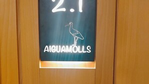 Un letrero con el número 2.1 y la palabra 'AIGUAMOLLS' sobre un fondo de madera.