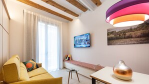 Una sala moderna con sofá, una mesa de vidrio, una mesa auxiliar, un televisor montado en la pared y una lámpara decorativa.