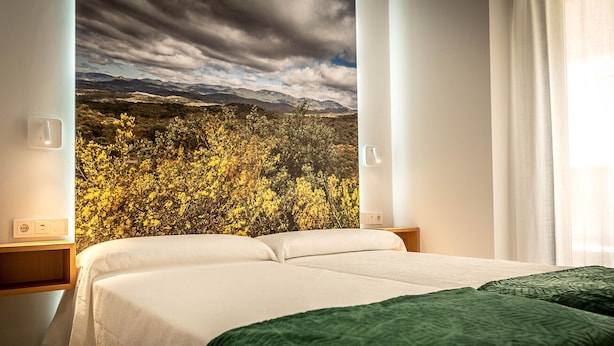 A hotel room with a bed, a nightstand, a wall-mounted light, and a window with curtains.