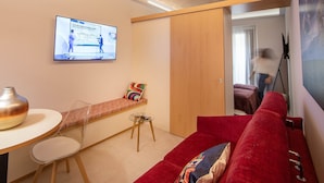 Un salon moderne avec un canapé rouge, une table en verre et un téléviseur diffusant un programme d’information.
