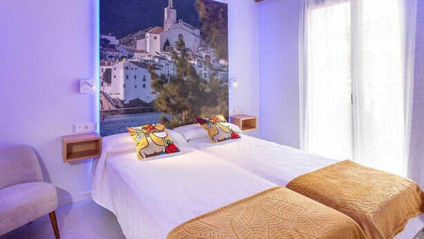A hotel room with a bed, a chair, a nightstand, a wall-mounted lamp, and a window with curtains. - 3-1 Cadaqués - Standard Apartment (Figueres)
