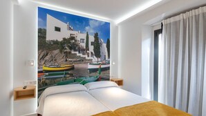 Ein Hotelzimmer mit Bett, Nachttisch, Wandleuchte, Fenster mit Vorhängen und einem Wandbild von Booten und Gebäuden.