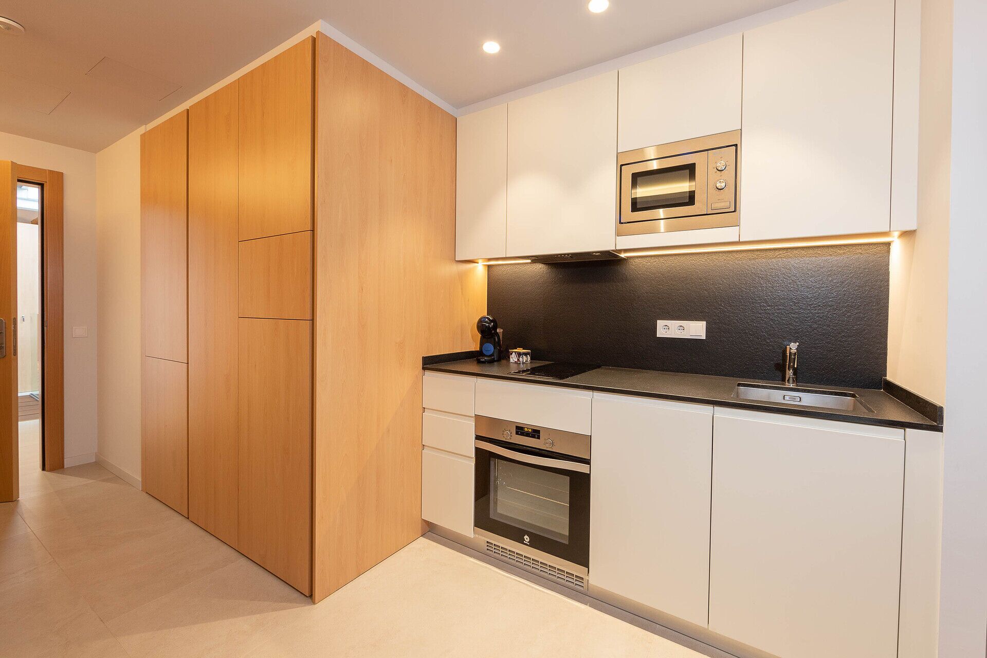 A modern kitchen with wooden cabinets, a built-in oven, a microwave, and a coffee maker.