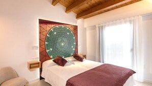 Ein Schlafzimmer mit einem großen Bett, einem Kopfteil mit geometrischem Muster, einem Nachttisch, einem Sessel und einem Fenster mit Vorhängen.