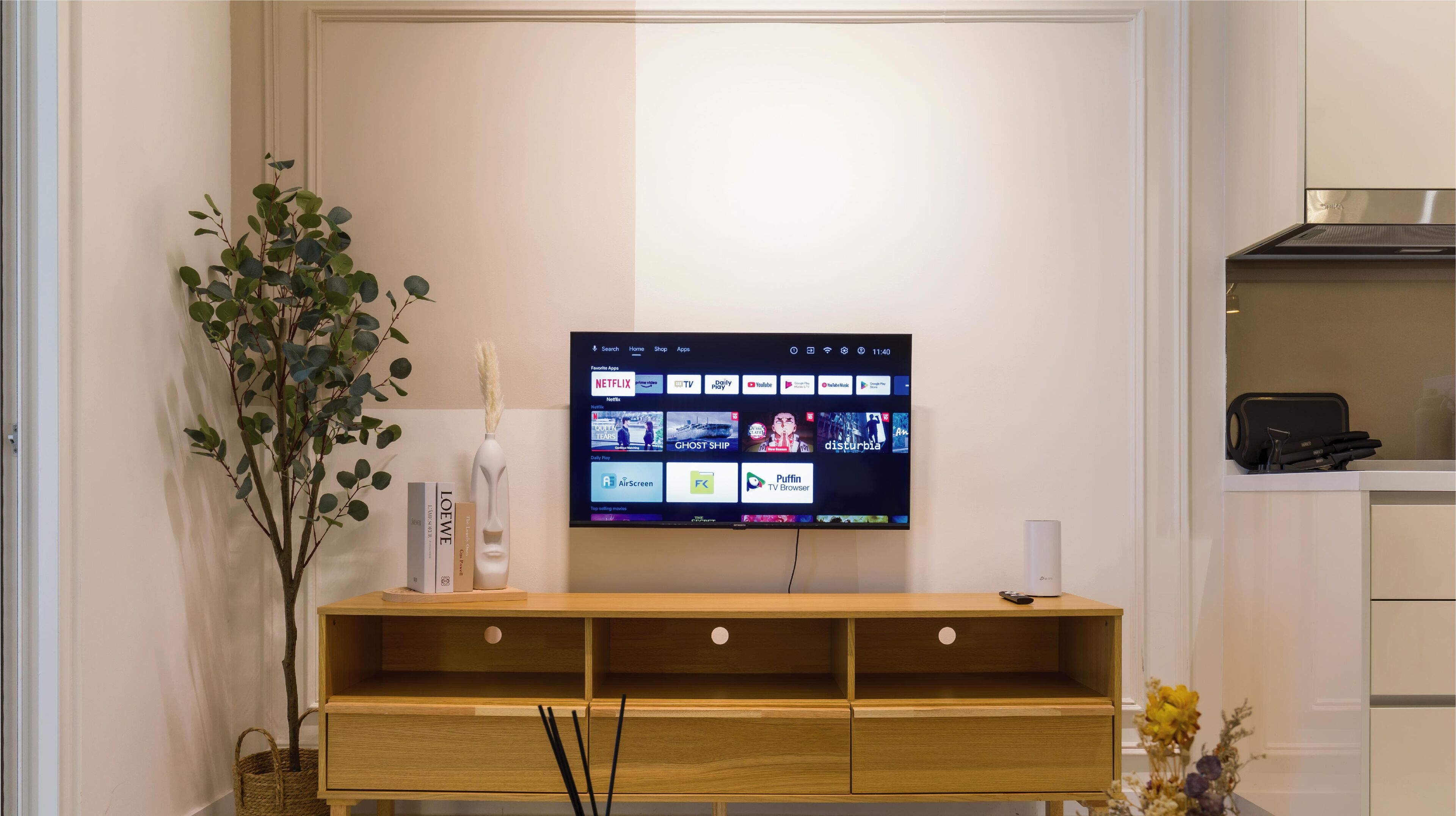 Una sala de estar moderna con un televisor de pantalla plana montado en la pared, un mueble de madera debajo y una planta en maceta a la izquierda.