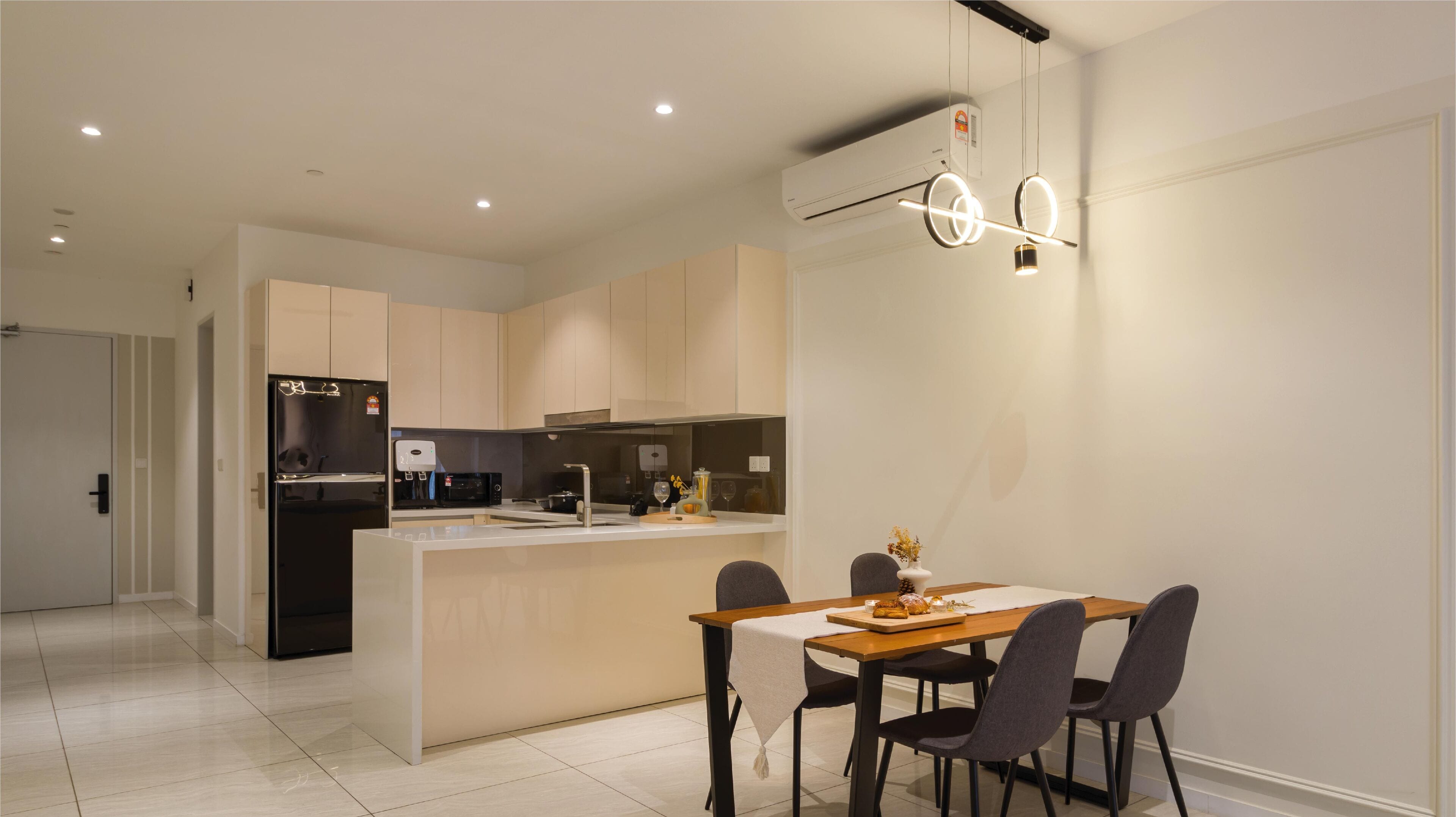 Una cocina moderna con una isla central, un comedor con mesa y sillas, e iluminación empotrada en el techo.