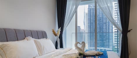 A hotel room with a large bed, a view of tall buildings, and sheer curtains.