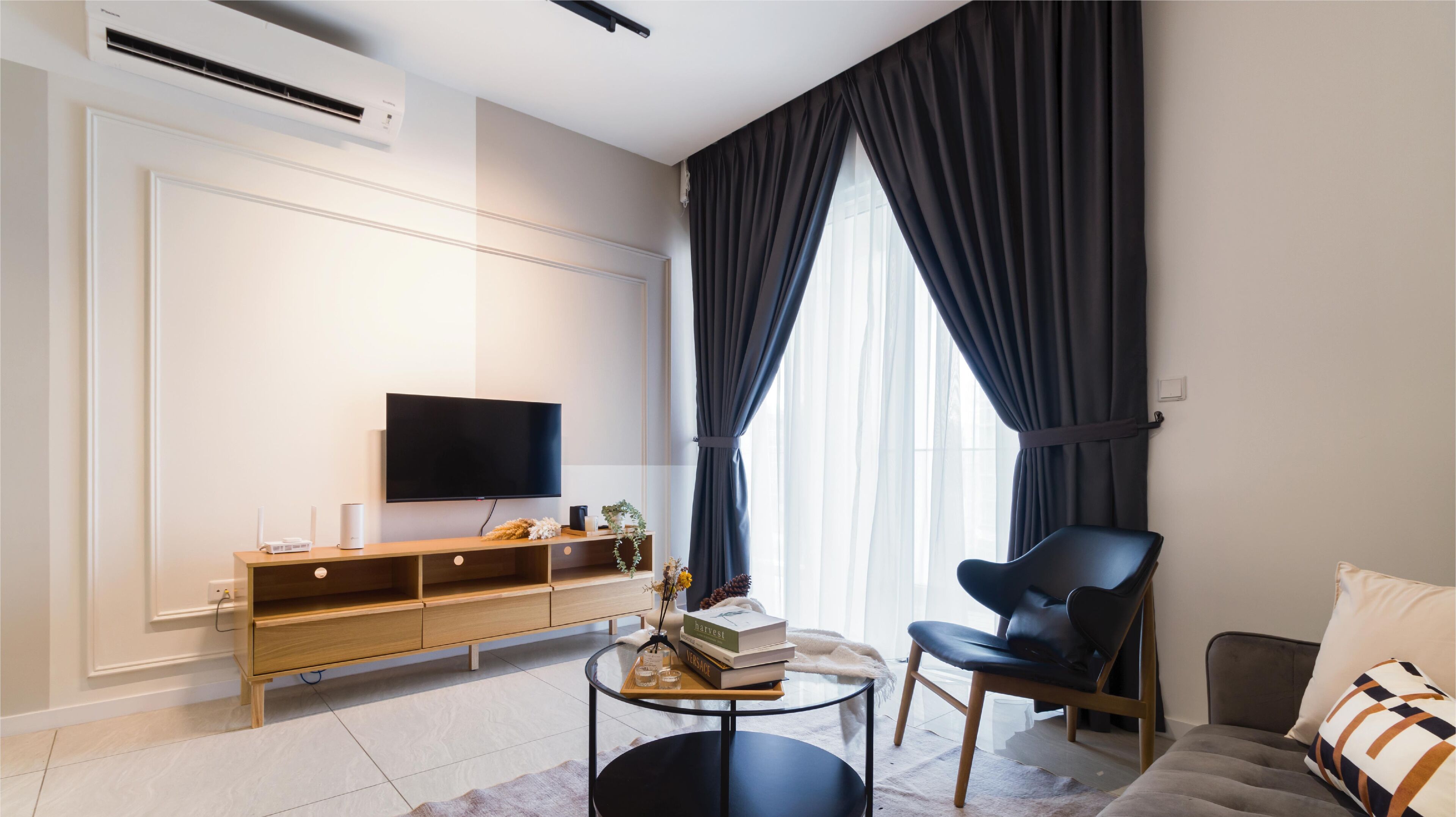 A modern living room with a flat-screen TV, a wooden console table, a black leather chair, and a sofa with patterned cushions.