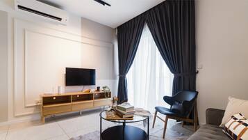 A modern living room with a flat-screen TV, a wooden console table, a black leather chair, and a sofa with patterned cushions.