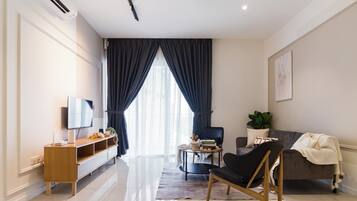 Un salon moderne avec un téléviseur à écran plat, un meuble de rangement en bois, une table basse ronde, un fauteuil noir, un canapé gris et une grande fenêtre avec des rideaux foncés.