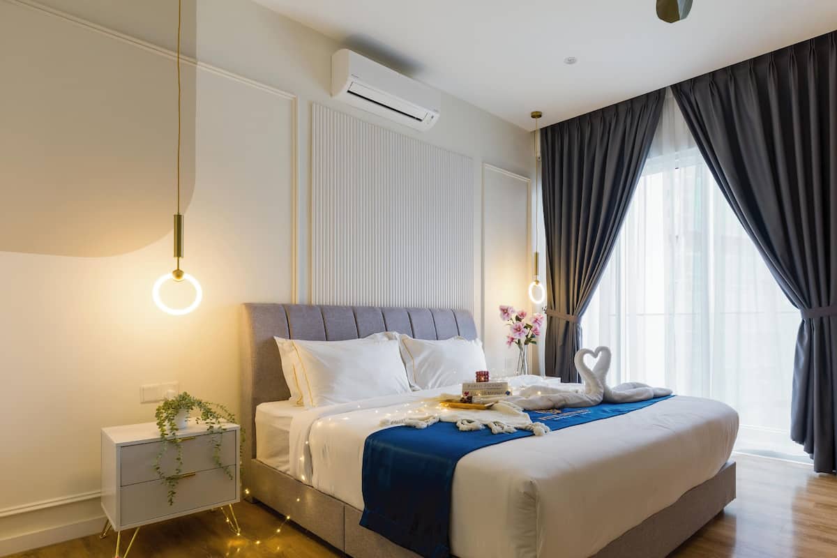 A modern bedroom with a bed, bedside tables, a nightstand, a potted plant, and a window with curtains.