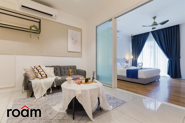 A modern living room with a sofa, a coffee table, and a bed with blue curtains. - Quill Residences KLCC, Five Senses (Kuala Lumpur)