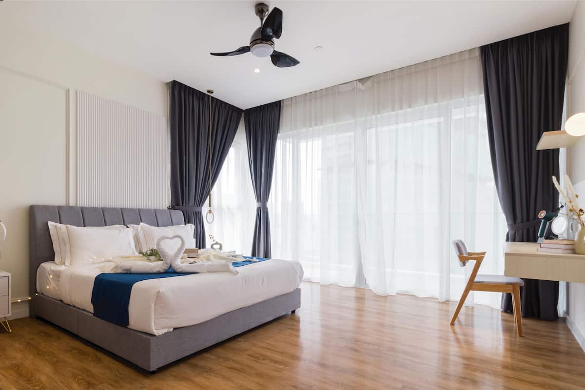 A modern bedroom with a bed, bedside table, desk, chair, and a ceiling fan.