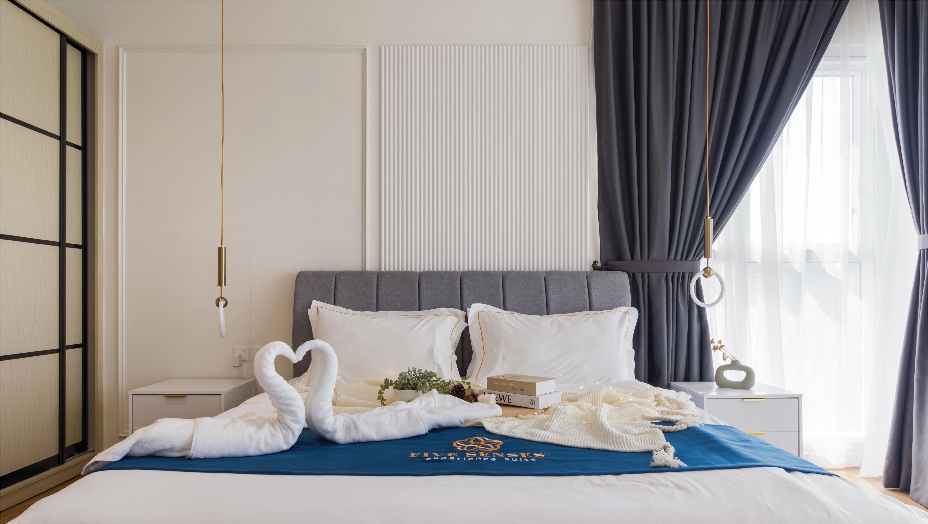 A neatly made bed with a blue blanket, a heart-shaped towel arrangement, and a book titled "The Earth, Our Home."