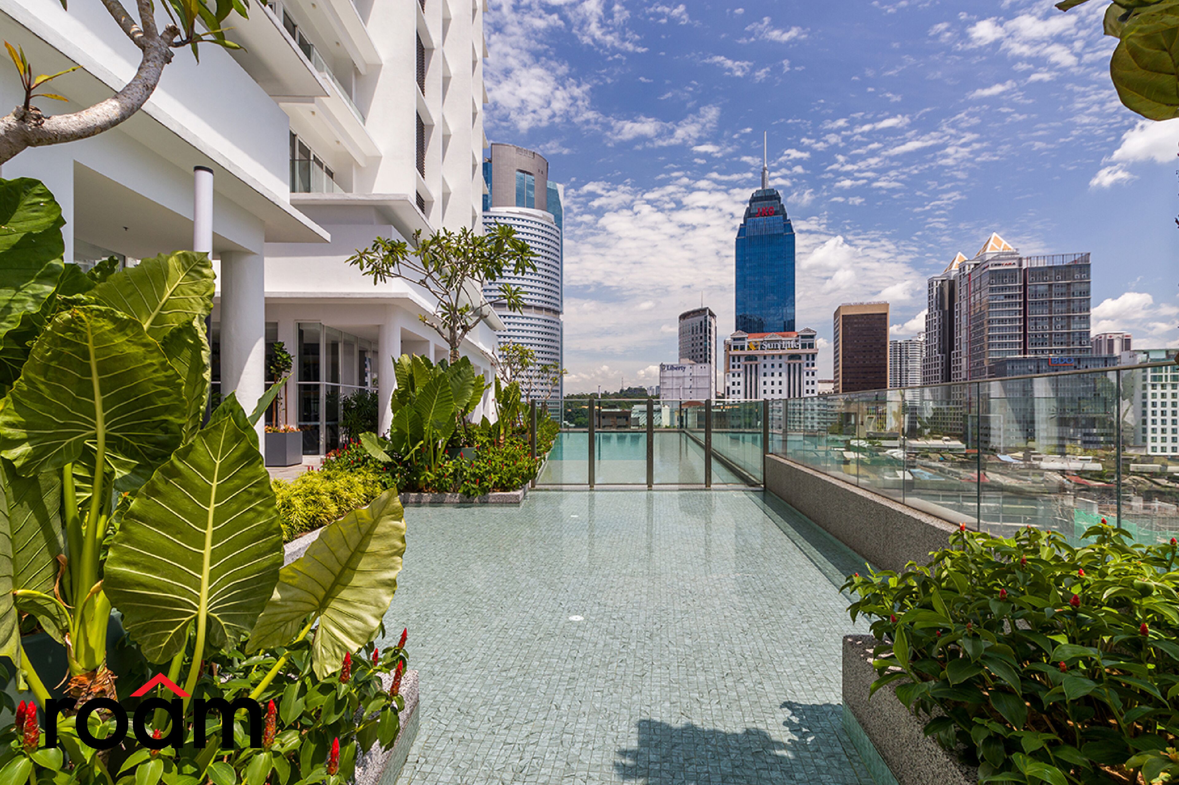 Una piscina en la azotea con vista a la ciudad, rodeada de exuberante vegetación y arquitectura moderna.