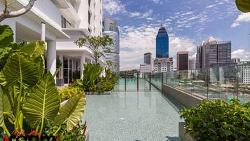 Una piscina en la azotea con vista a la ciudad, rodeada de exuberante vegetación y arquitectura moderna.