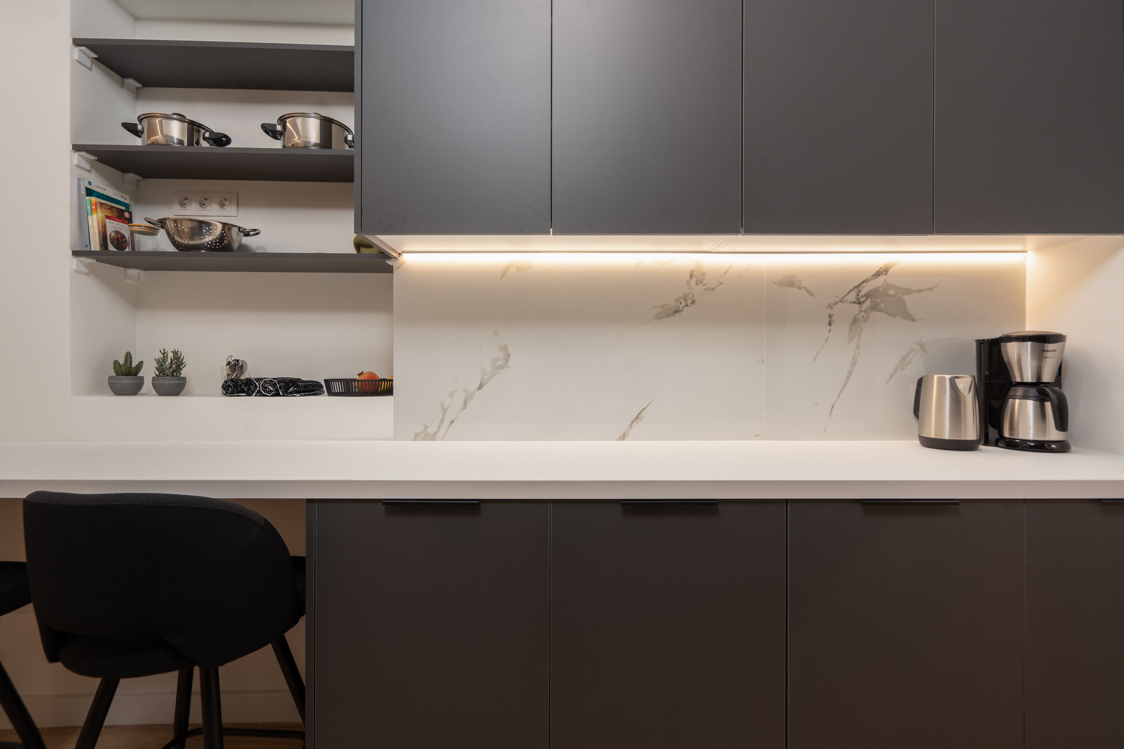 A modern kitchen with grey cabinets, a white countertop, and a marble backsplash. There are two coffee makers on the counter.
