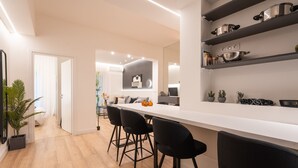 A modern kitchen with a white countertop, black bar stools, and shelves with kitchenware. - Exclusive and Deluxe Apartment in Athens (Athens)