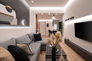Un salon moderne avec un canapé d’angle gris, une table basse agrémentée d’objets décoratifs, un téléviseur à écran plat fixé au mur et un design minimaliste avec des spots encastrés au plafond.