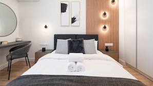 A modern hotel room with a neatly made bed, a desk with a chair, a small potted plant, and a wall-mounted air conditioner. - Exclusive and Deluxe Apartment in Athens (Athens)