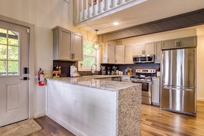 A modern kitchen with a central island, stainless steel appliances, and a herringbone tile backsplash.