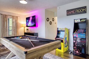 A pool table with balls, a neon sign reading 'GAME ROOM,' and arcade machines.