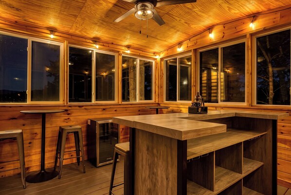 A wooden interior with large windows, a bar area, and a ceiling fan.