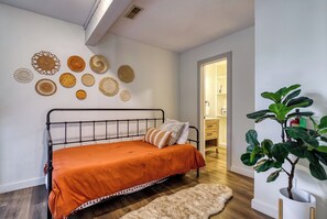 Une chambre à coucher avec un lit, un mur orné de motifs circulaires décoratifs, une plante et une porte donnant sur une autre pièce.