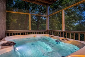 Un bain à remous doté d’une terrasse en bois et de panneaux en treillis, entouré d’arbres.
