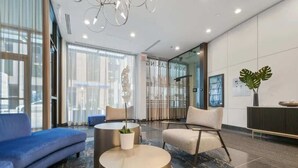 Um hall moderno com um sofá azul, uma poltrona bege e uma mesa redonda com uma planta.