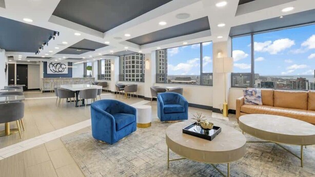 Uma área de estar moderna com assentos, mesa de centro e grandes janelas com vista para a cidade.