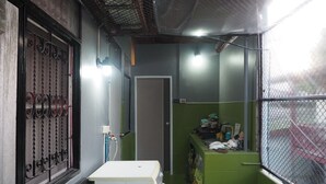 A narrow, enclosed space with a green wall, a white washing machine, a metal gate, and a window with a mesh screen. - Doctor Alien Hostel (Bangkok)