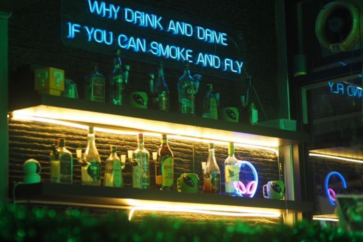 En bar med en neonreklamskylt som visar texten: ”VARFÖR DRIKA OCH KÖRA NÄR DU KAN RÖKA OCH FLYGA?”