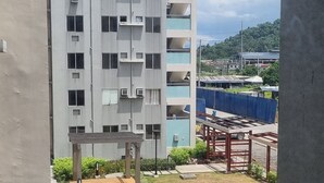 A modern building with multiple floors, a courtyard with greenery, and a clear view of the sea in the background. - Cozy Condo: Clean, 24/7 Security, 
Near S&R Davao and some Universities/Schools (Davao City)