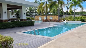 A rectangular swimming pool with a wooden deck and metal ladders, surrounded by lush greenery and a stone wall. - Cozy Condo: Clean, 24/7 Security, 
Near S&R Davao and some Universities/Schools (Davao City)